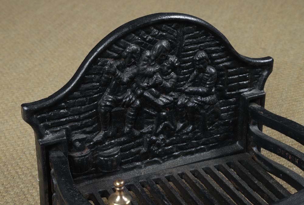 A black cast iron fire grate featuring an arched pictorial backplate, curved front bars, and brass urn finials on the front posts. View VIII