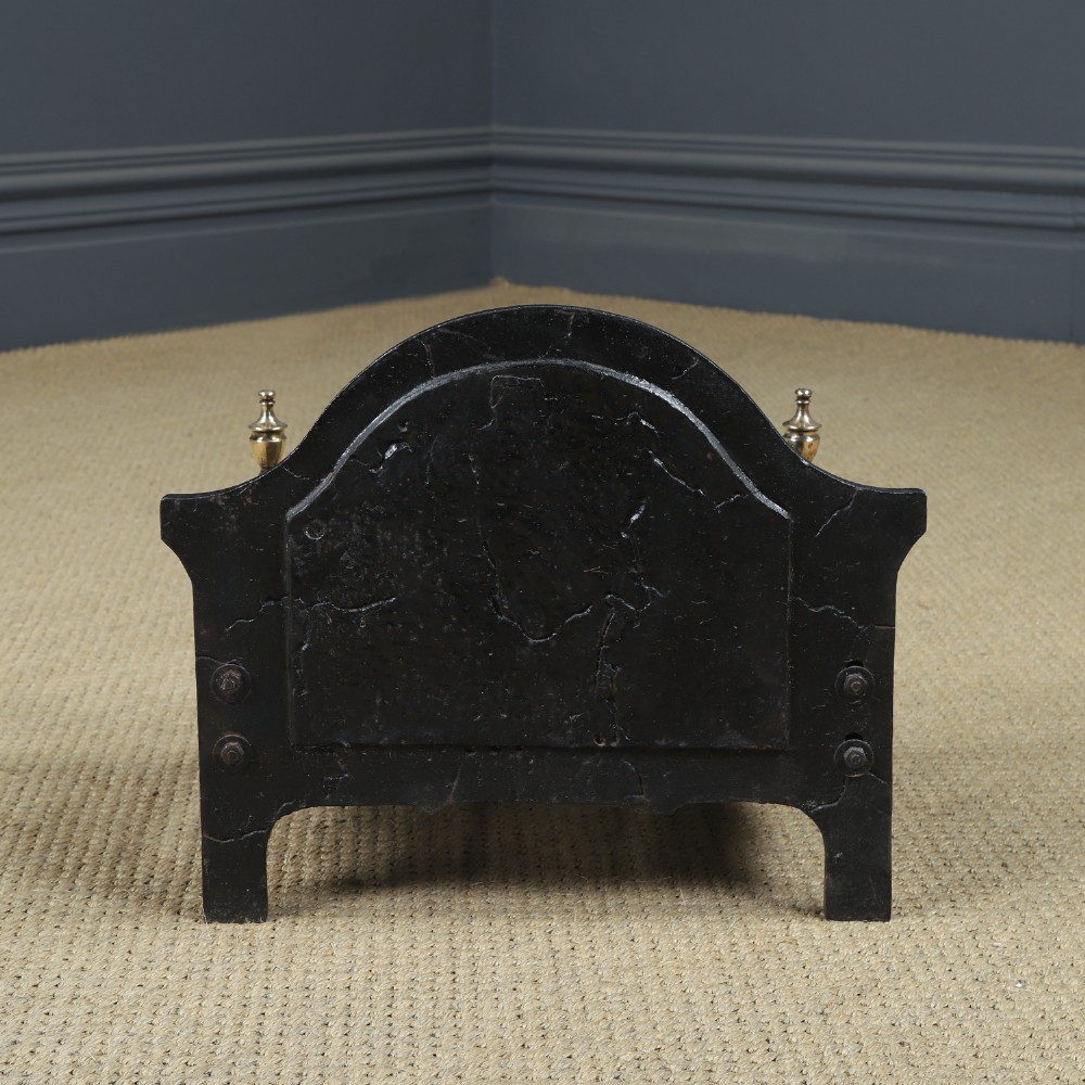 A black cast iron fire grate featuring an arched pictorial backplate, curved front bars, and brass urn finials on the front posts. View XIII