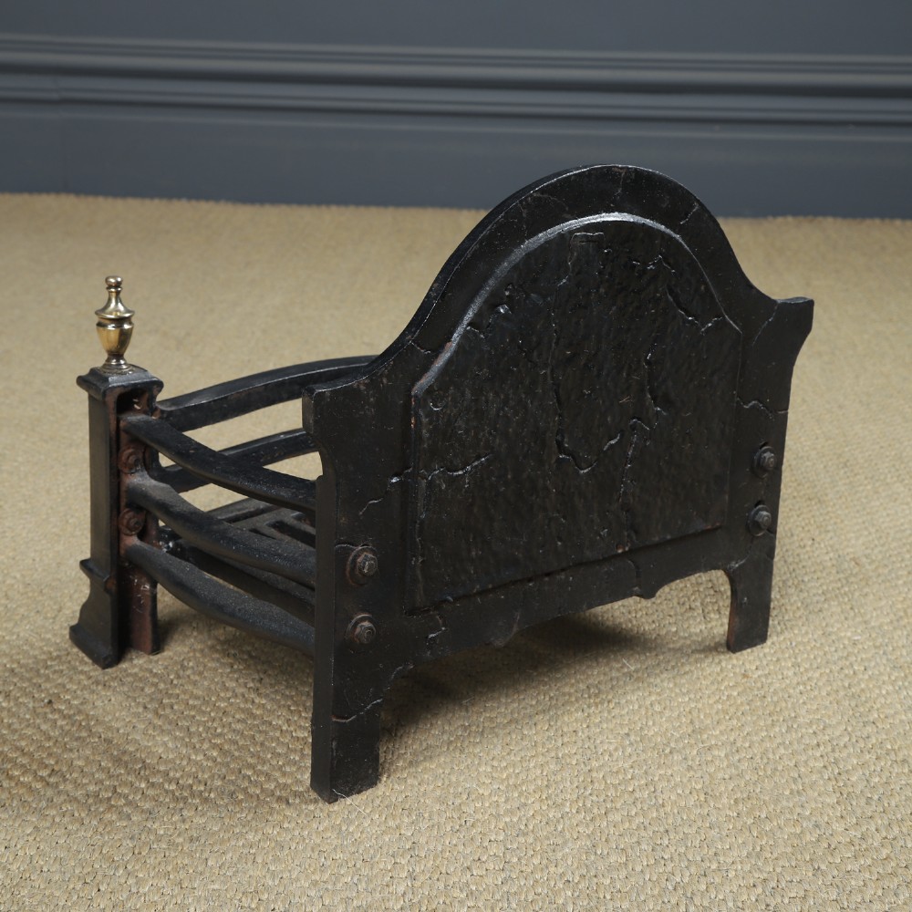 A black cast iron fire grate featuring an arched pictorial backplate, curved front bars, and brass urn finials on the front posts. View XIV