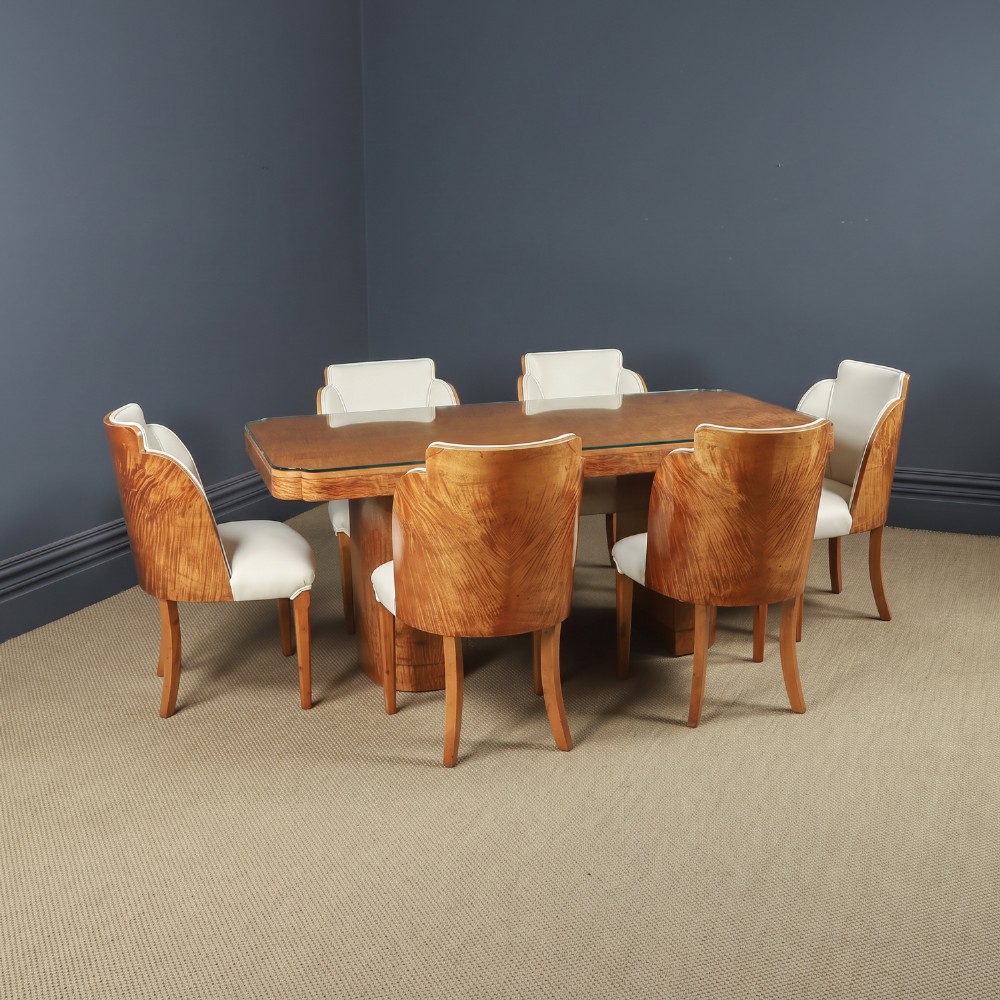 An English Art Deco dining suite featuring a rectangular satinwood and maple dining table with a glass top and six cream leather upholstered chairs with curved veneered backs.