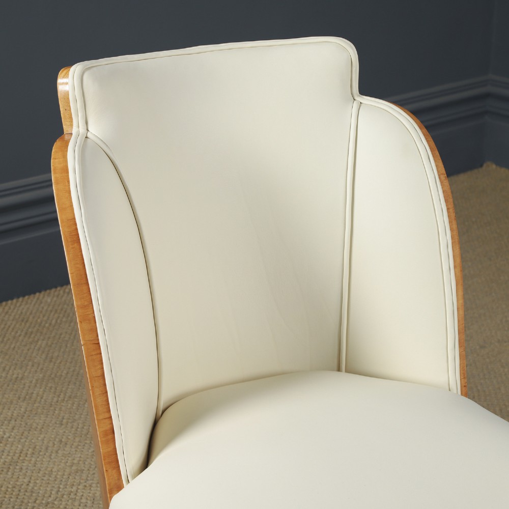 An English Art Deco dining suite featuring a rectangular satinwood and maple dining table with a glass top and six cream leather upholstered chairs with curved veneered backs. View IX