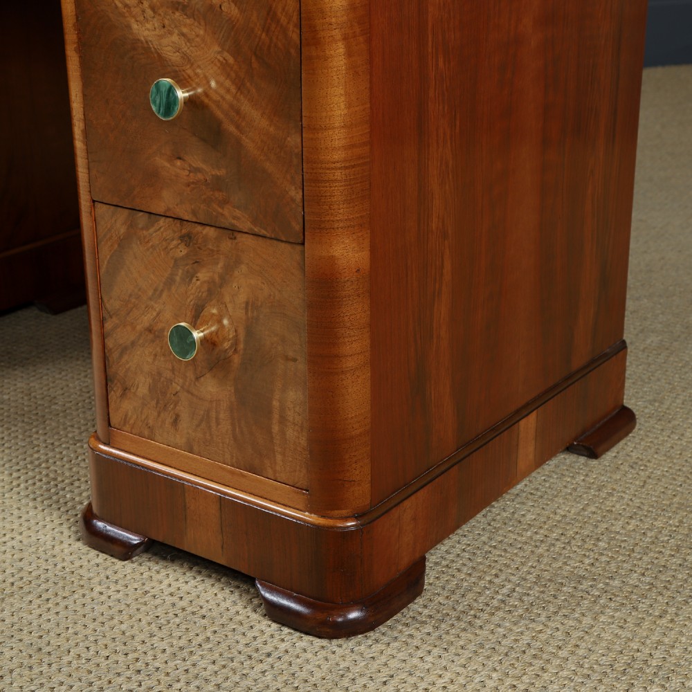 An Art Deco burr walnut pedestal writing desk with green circular knobs and a fitted glass top. View IX