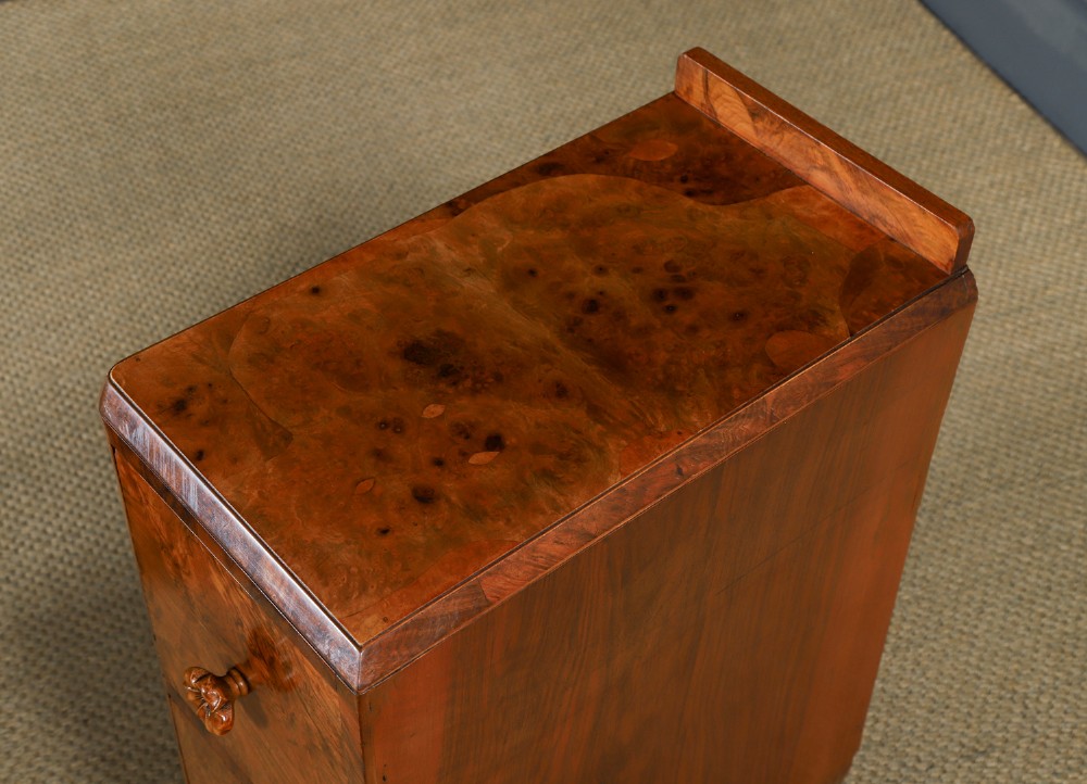 A pair of narrow Art Deco burr walnut bedside cabinets featuring two drawers with carved circular handles and a low back ledge. View VI