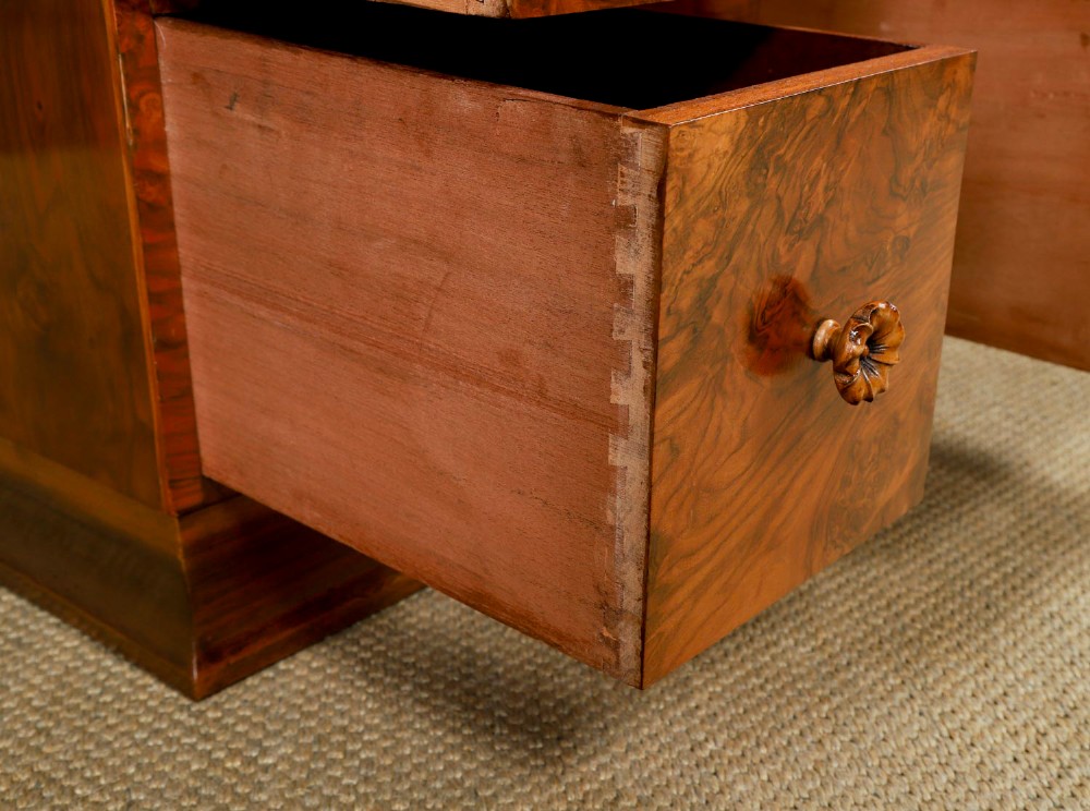 A pair of narrow Art Deco burr walnut bedside cabinets featuring two drawers with carved circular handles and a low back ledge. View X