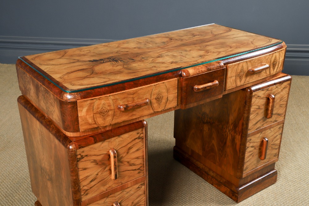 An Art Deco walnut and burr elm pedestal desk featuring stepped side pedestals, bookmatched wood veneers, wooden handles, and a fitted glass top. View II