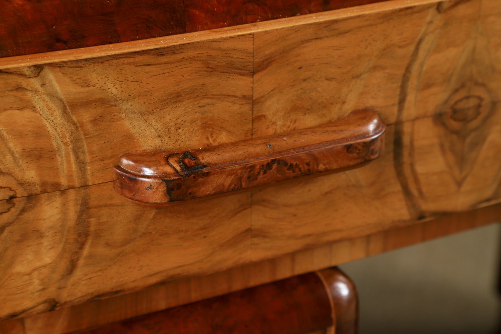 An Art Deco walnut and burr elm pedestal desk featuring stepped side pedestals, bookmatched wood veneers, wooden handles, and a fitted glass top. View V