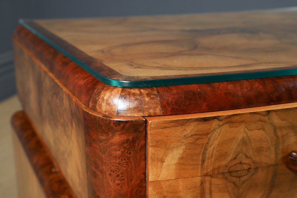 An Art Deco walnut and burr elm pedestal desk featuring stepped side pedestals, bookmatched wood veneers, wooden handles, and a fitted glass top. View VIII