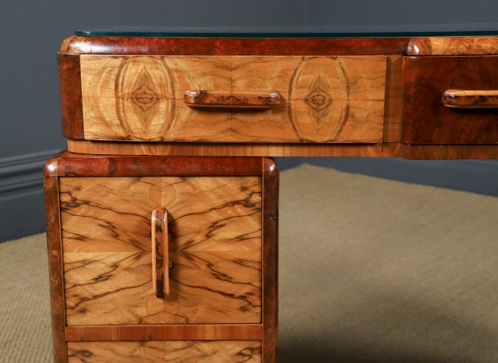 An Art Deco walnut and burr elm pedestal desk featuring stepped side pedestals, bookmatched wood veneers, wooden handles, and a fitted glass top. View IX