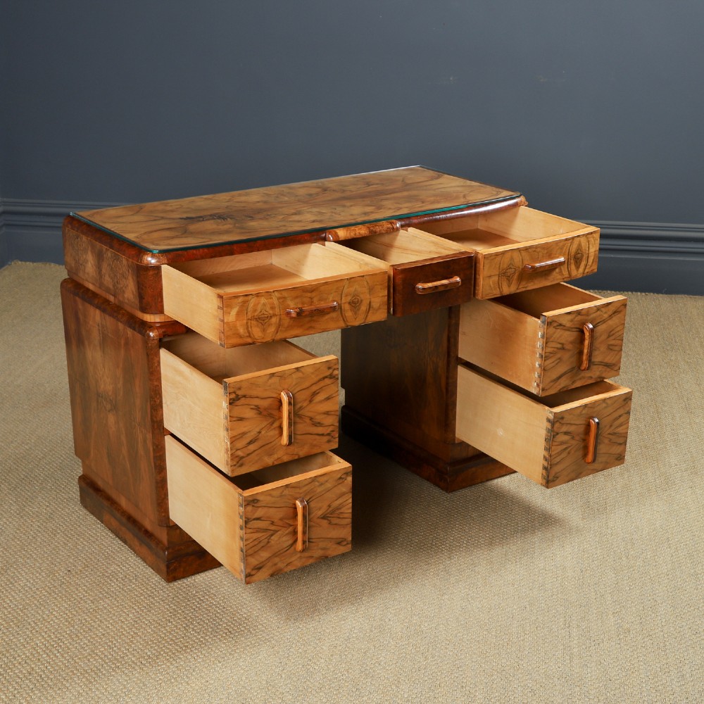 An Art Deco walnut and burr elm pedestal desk featuring stepped side pedestals, bookmatched wood veneers, wooden handles, and a fitted glass top. View XI