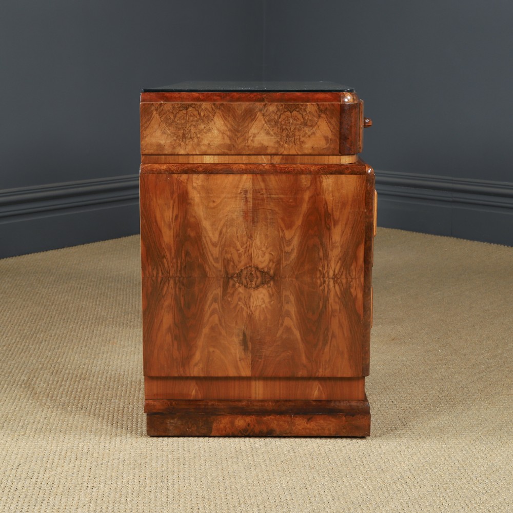 An Art Deco walnut and burr elm pedestal desk featuring stepped side pedestals, bookmatched wood veneers, wooden handles, and a fitted glass top. View XIII