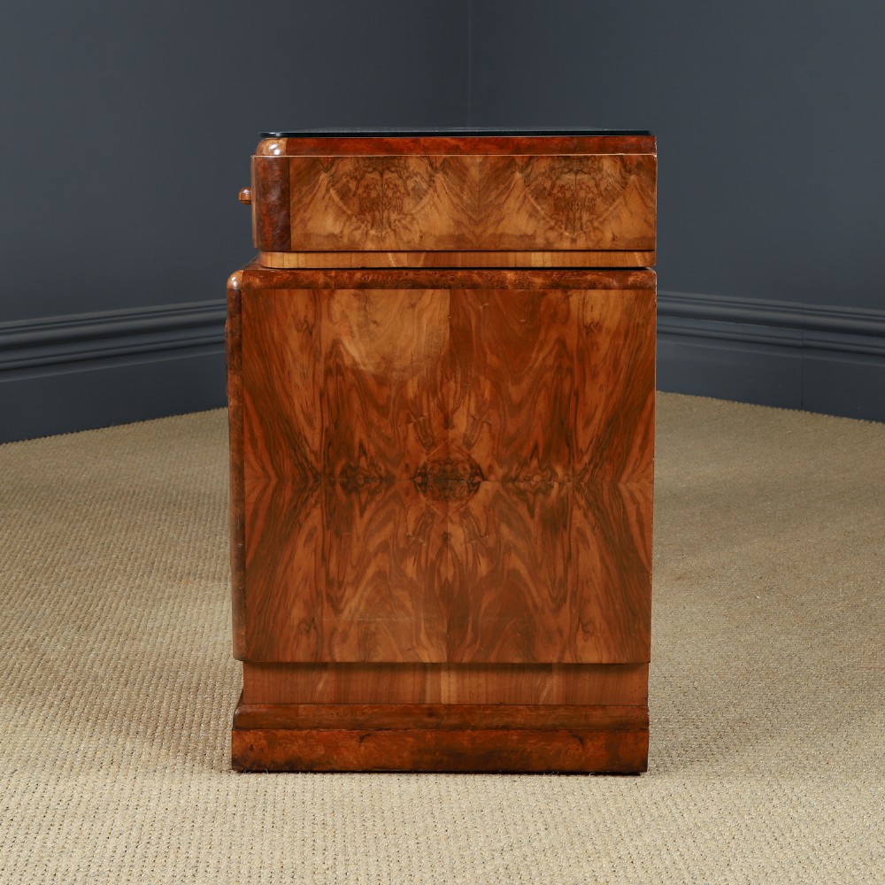 An Art Deco walnut and burr elm pedestal desk featuring stepped side pedestals, bookmatched wood veneers, wooden handles, and a fitted glass top. View XIV