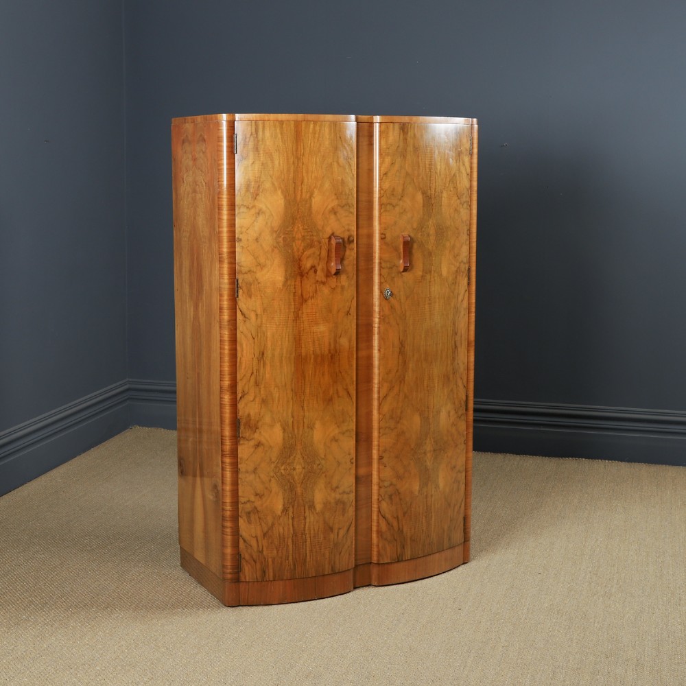 An Art Deco walnut two door wardrobe featuring a bow front design, carved wood handles, and figured timber grain.