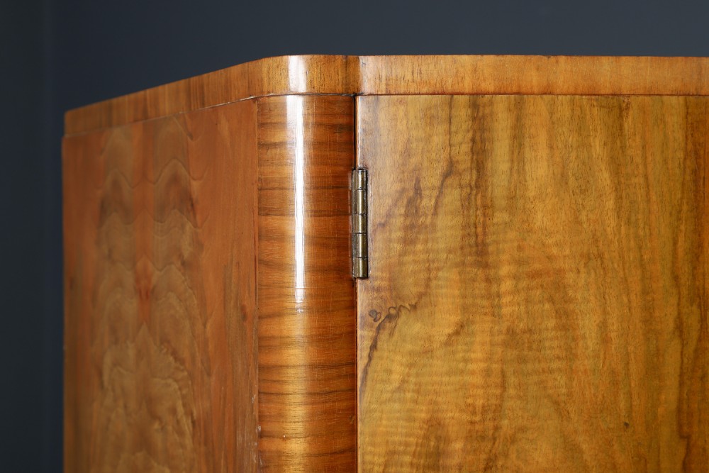 An Art Deco walnut two door wardrobe featuring a bow front design, carved wood handles, and figured timber grain. View V