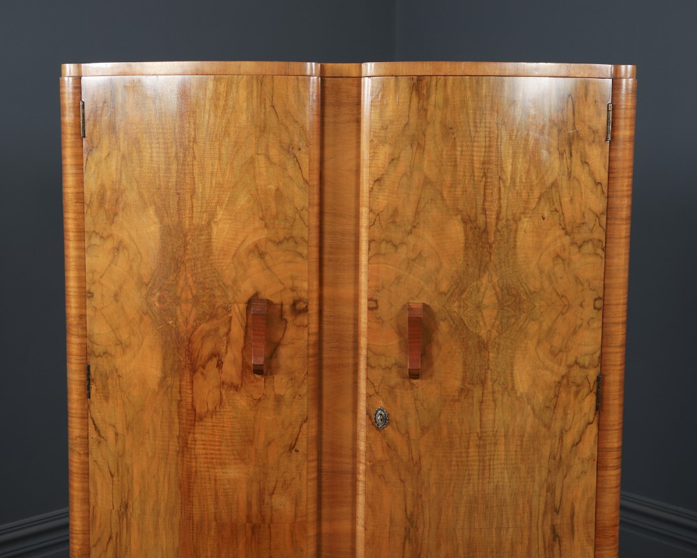 An Art Deco walnut two door wardrobe featuring a bow front design, carved wood handles, and figured timber grain. View VI