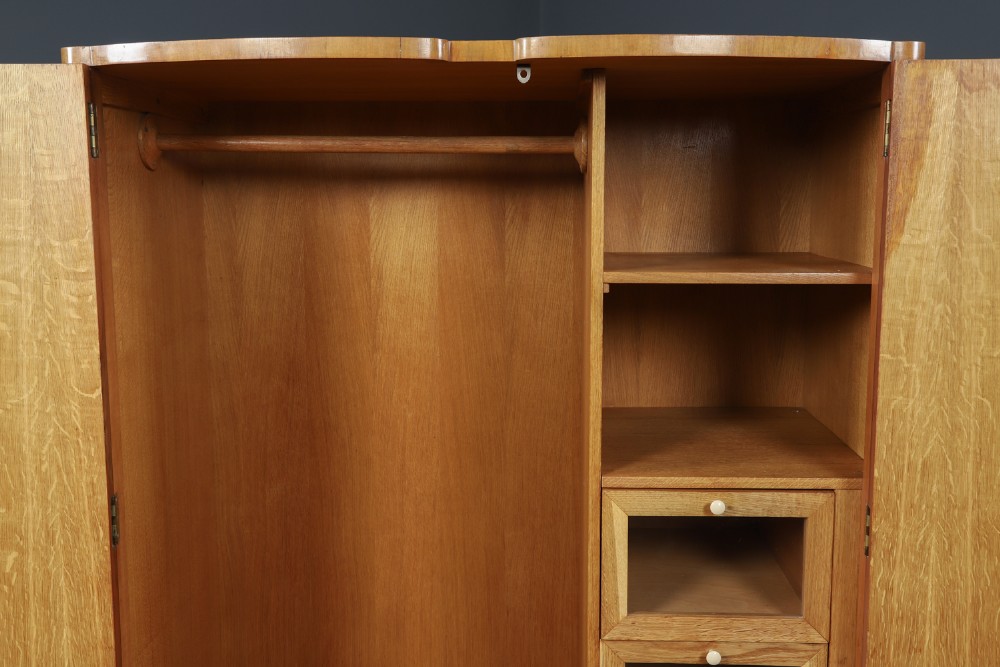 An Art Deco walnut two door wardrobe featuring a bow front design, carved wood handles, and figured timber grain. View IX