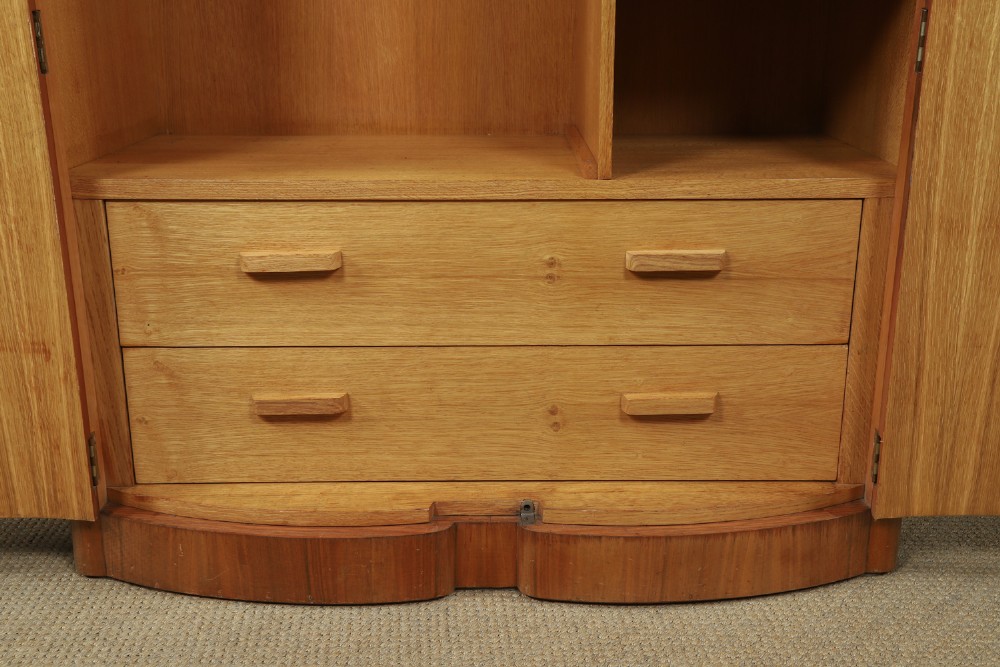 An Art Deco walnut two door wardrobe featuring a bow front design, carved wood handles, and figured timber grain. View X