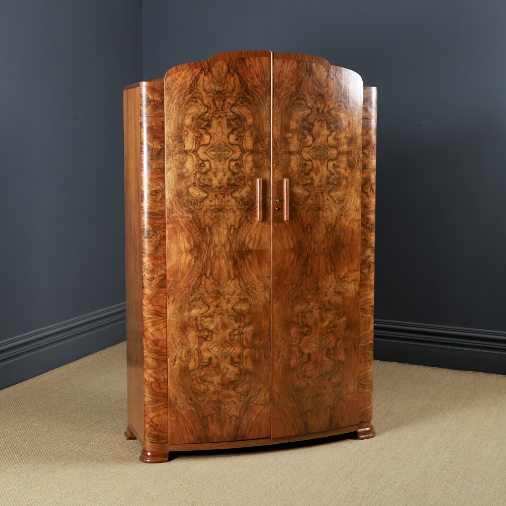 An Art Deco two door wardrobe crafted from warm brown figured walnut veneer with a gently curved bow front and wooden vertical handles.
