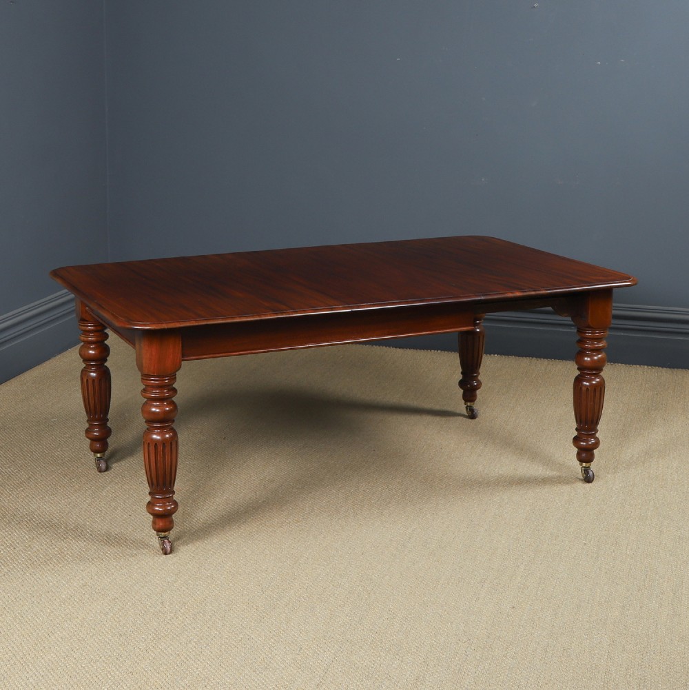 A Victorian mahogany extending dining table with a rectangular top, rounded corners, and turned fluted legs set on brass castors.