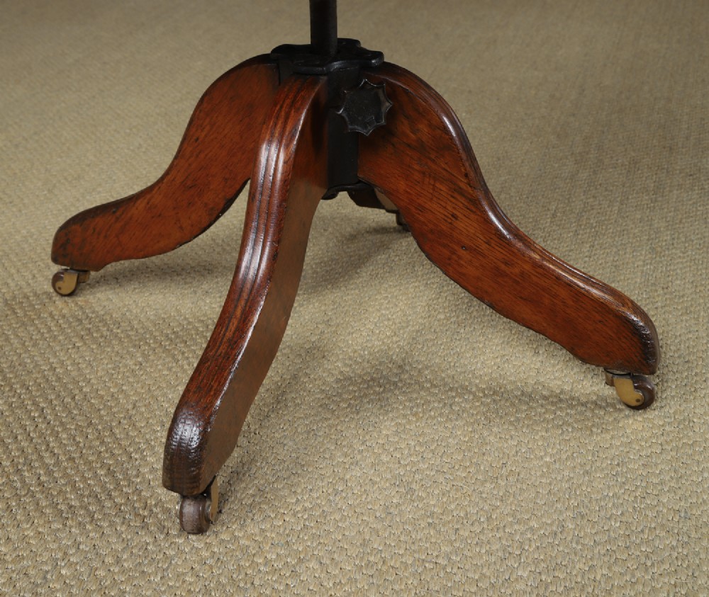An Edwardian oak revolving desk armchair featuring a carved pierced back splat, green leather upholstered seat with close studding, and a four-point swivel base on brass castors. View IV