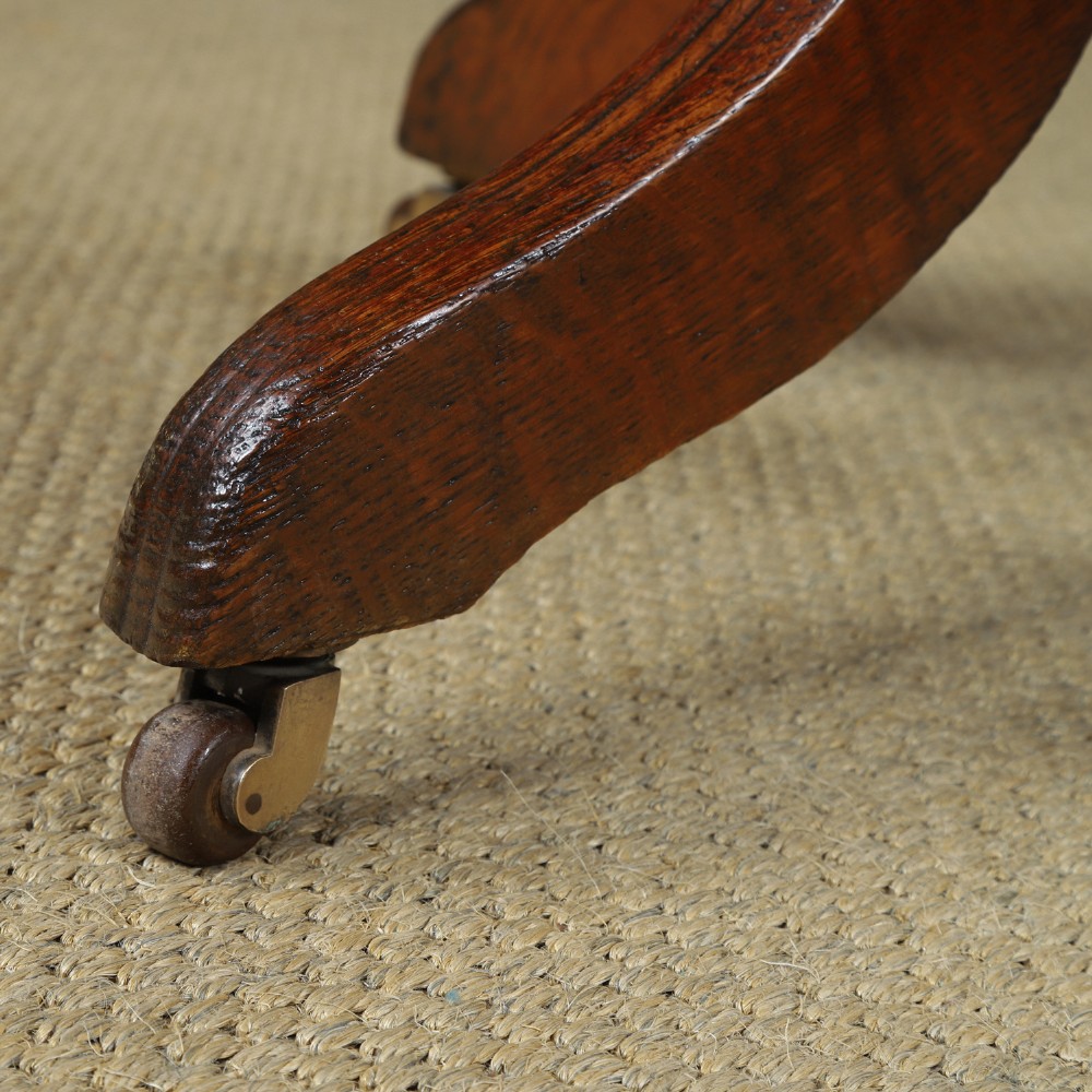 An Edwardian oak revolving desk armchair featuring a carved pierced back splat, green leather upholstered seat with close studding, and a four-point swivel base on brass castors. View V