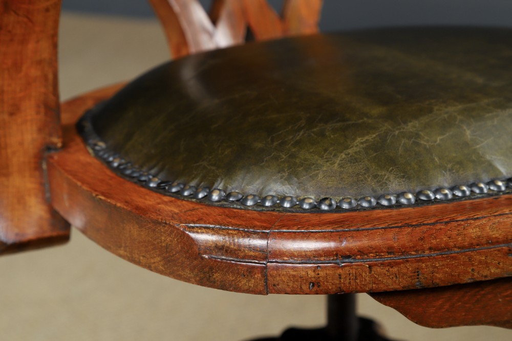 An Edwardian oak revolving desk armchair featuring a carved pierced back splat, green leather upholstered seat with close studding, and a four-point swivel base on brass castors. View VII