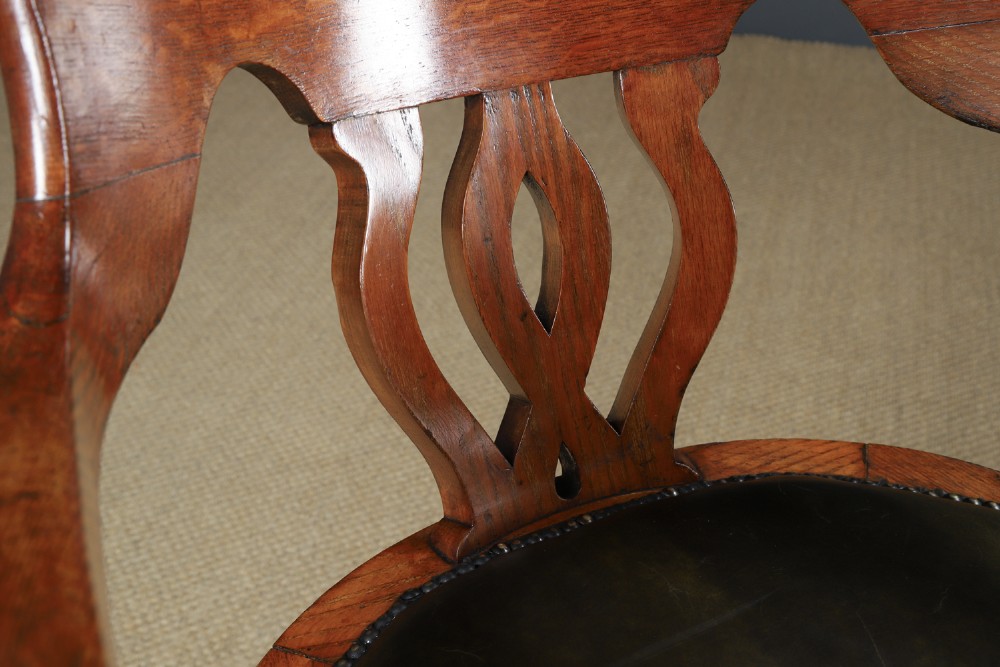 An Edwardian oak revolving desk armchair featuring a carved pierced back splat, green leather upholstered seat with close studding, and a four-point swivel base on brass castors. View VIII