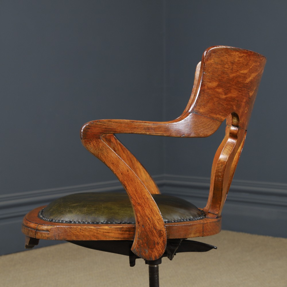 An Edwardian oak revolving desk armchair featuring a carved pierced back splat, green leather upholstered seat with close studding, and a four-point swivel base on brass castors. View IX