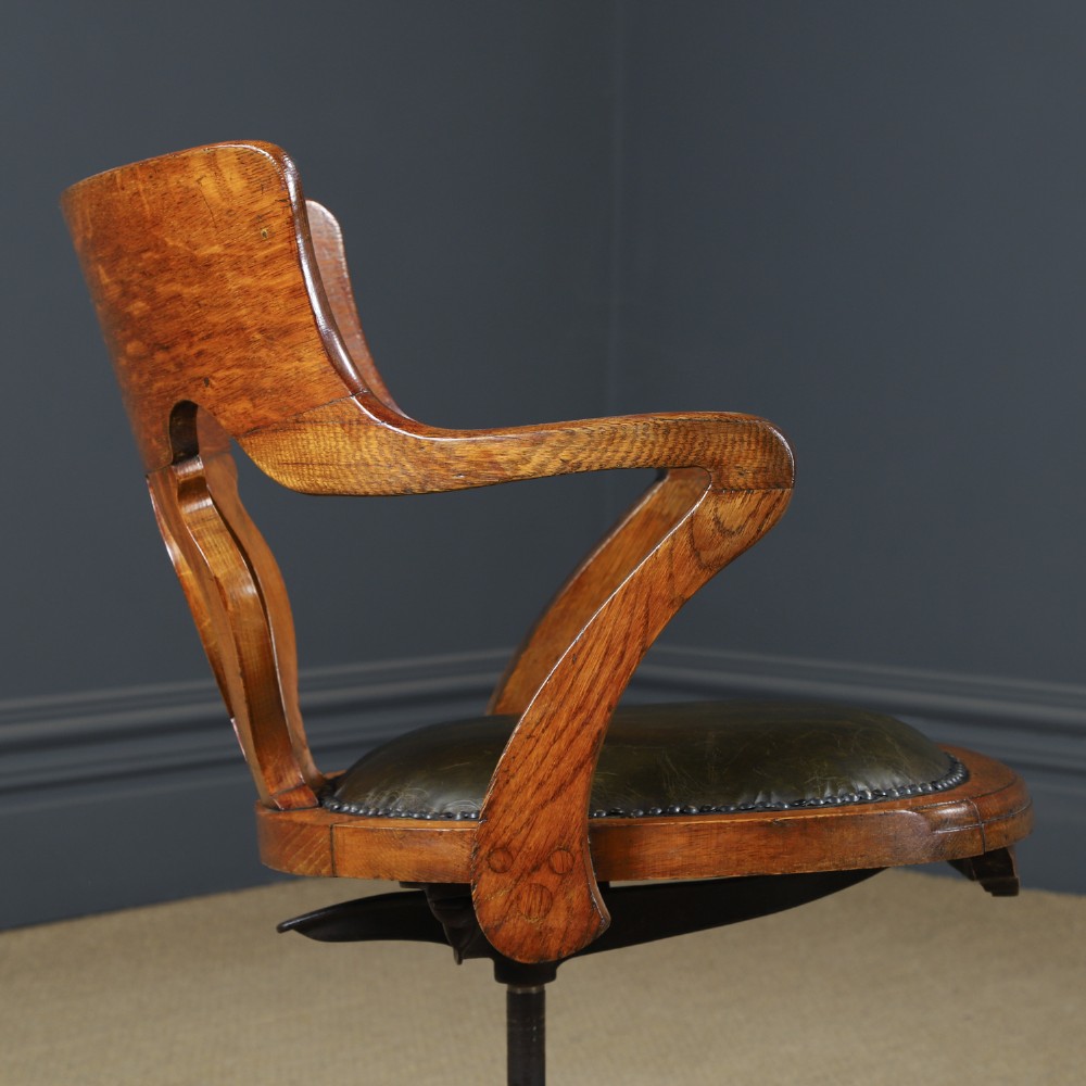 An Edwardian oak revolving desk armchair featuring a carved pierced back splat, green leather upholstered seat with close studding, and a four-point swivel base on brass castors. View X