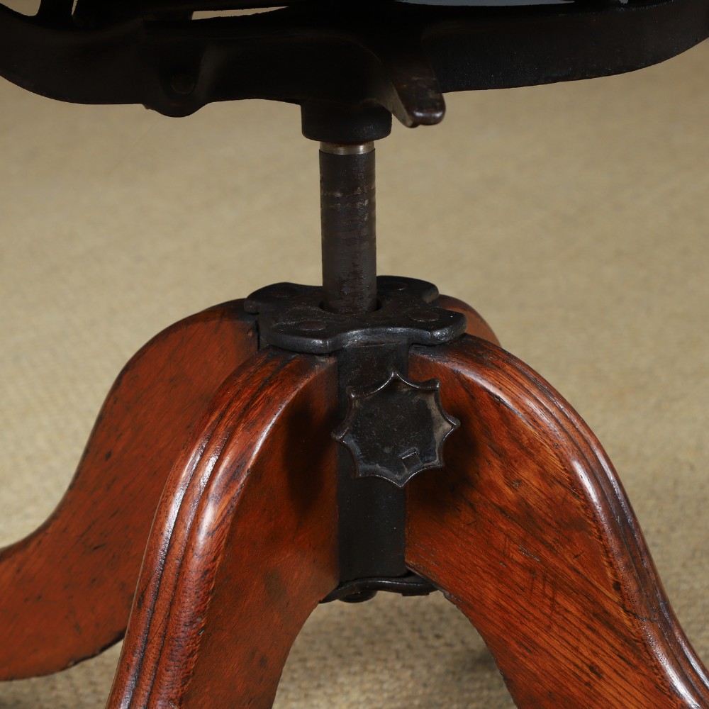 An Edwardian oak revolving desk armchair featuring a carved pierced back splat, green leather upholstered seat with close studding, and a four-point swivel base on brass castors. View XII