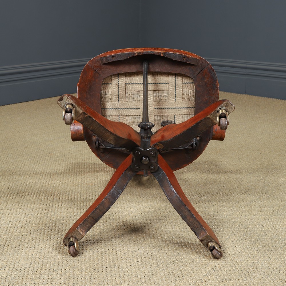 An Edwardian oak revolving desk armchair featuring a carved pierced back splat, green leather upholstered seat with close studding, and a four-point swivel base on brass castors. View XIII