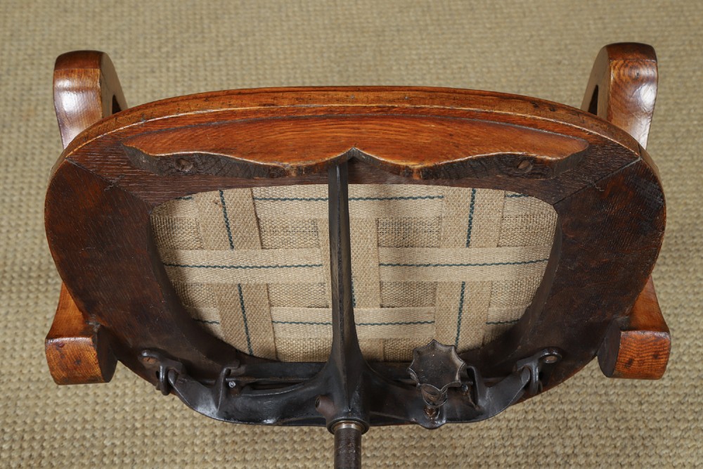 An Edwardian oak revolving desk armchair featuring a carved pierced back splat, green leather upholstered seat with close studding, and a four-point swivel base on brass castors. View XIV
