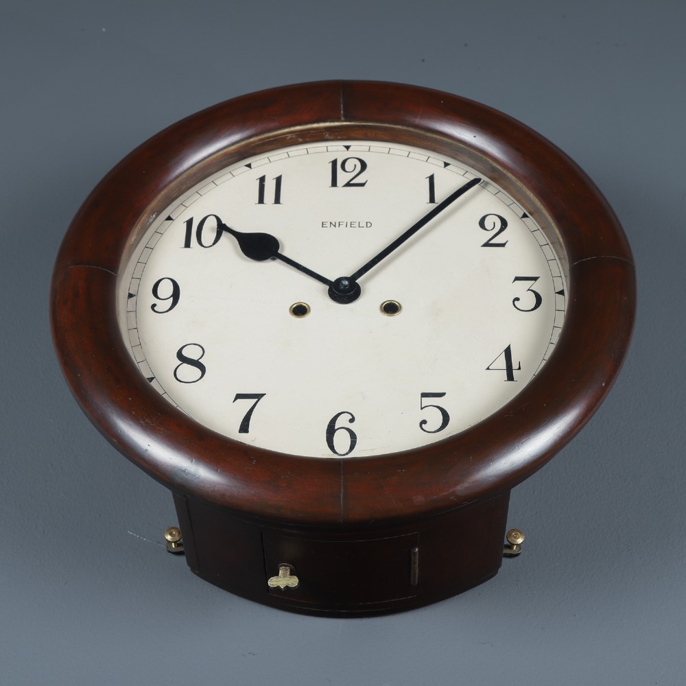 A circular mahogany wall clock with a cream dial, black Arabic numerals, black metal hands, two brass winding holes, and the Enfield maker name printed in the centre. View VIII