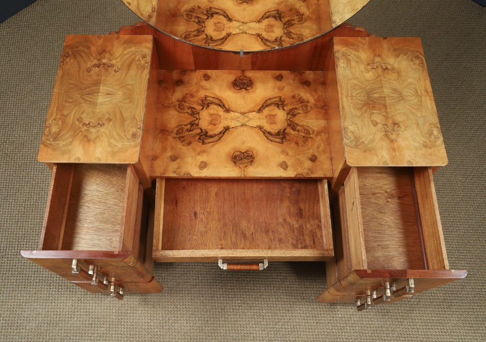 An Art Deco burr walnut pedestal dressing table featuring a large circular central mirror, a kneehole drawer, and three stacked drawers on each pedestal with vertical handles. View IX