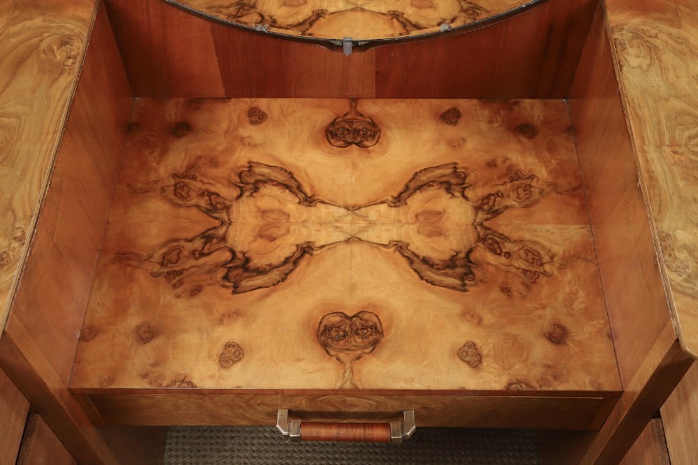 An Art Deco burr walnut pedestal dressing table featuring a large circular central mirror, a kneehole drawer, and three stacked drawers on each pedestal with vertical handles. View X