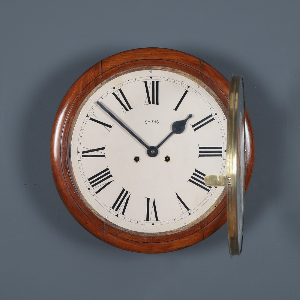 A circular Smiths antique wall clock with a turned mahogany wood surround, off-white dial with black Roman numerals, brass hinged bezel, and winding holes. View II