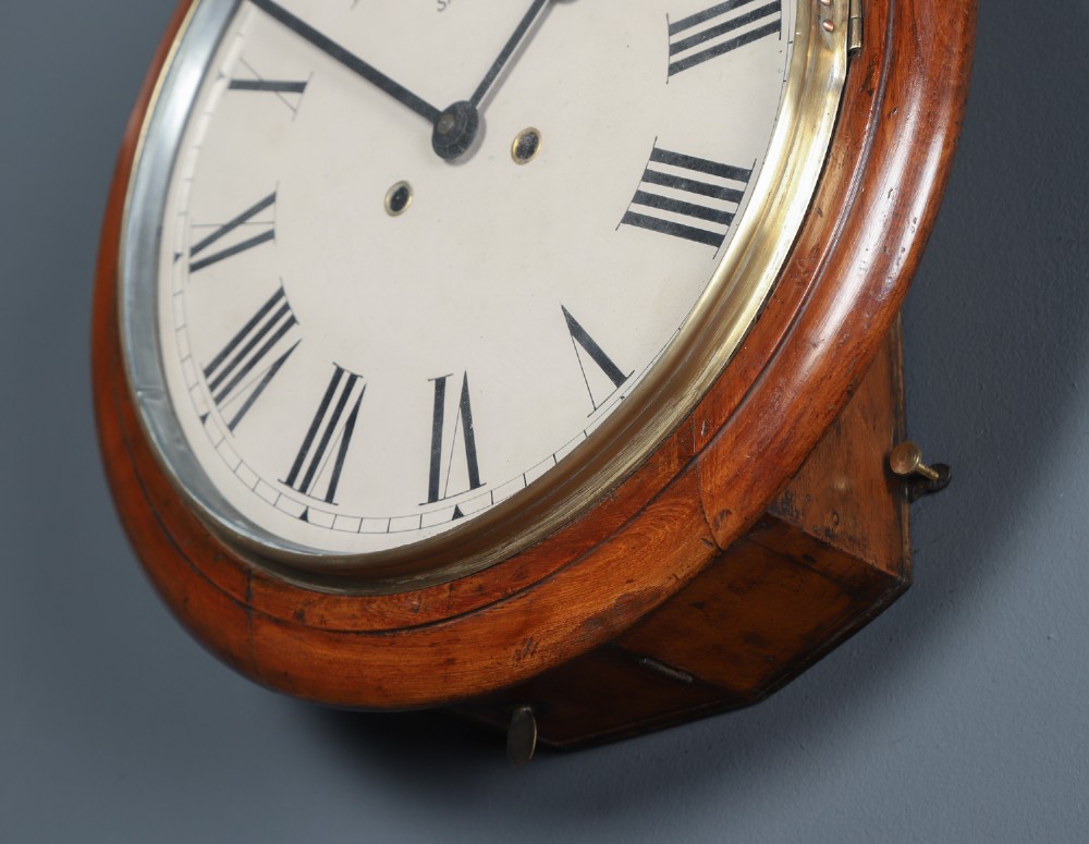 A circular Smiths antique wall clock with a turned mahogany wood surround, off-white dial with black Roman numerals, brass hinged bezel, and winding holes. View VIII