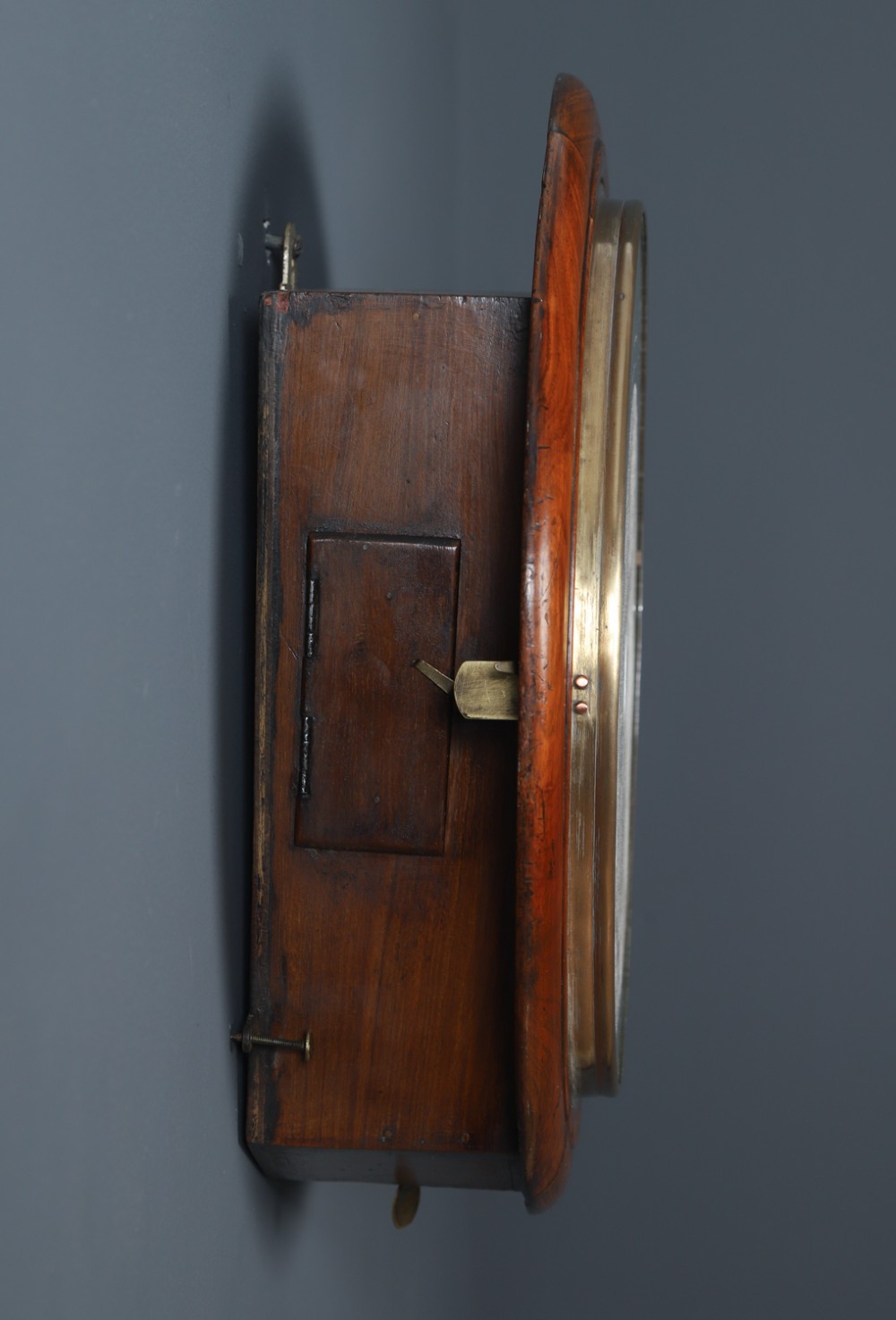 A circular Smiths antique wall clock with a turned mahogany wood surround, off-white dial with black Roman numerals, brass hinged bezel, and winding holes. View X