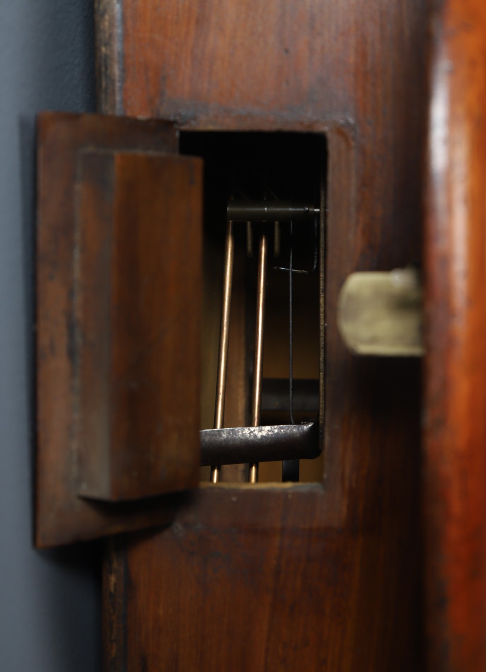 A circular Smiths antique wall clock with a turned mahogany wood surround, off-white dial with black Roman numerals, brass hinged bezel, and winding holes. View XII