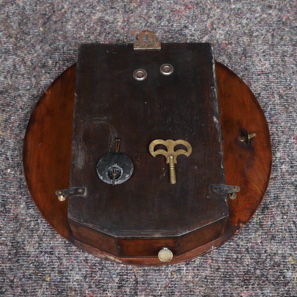 A circular Smiths antique wall clock with a turned mahogany wood surround, off-white dial with black Roman numerals, brass hinged bezel, and winding holes. View XIV