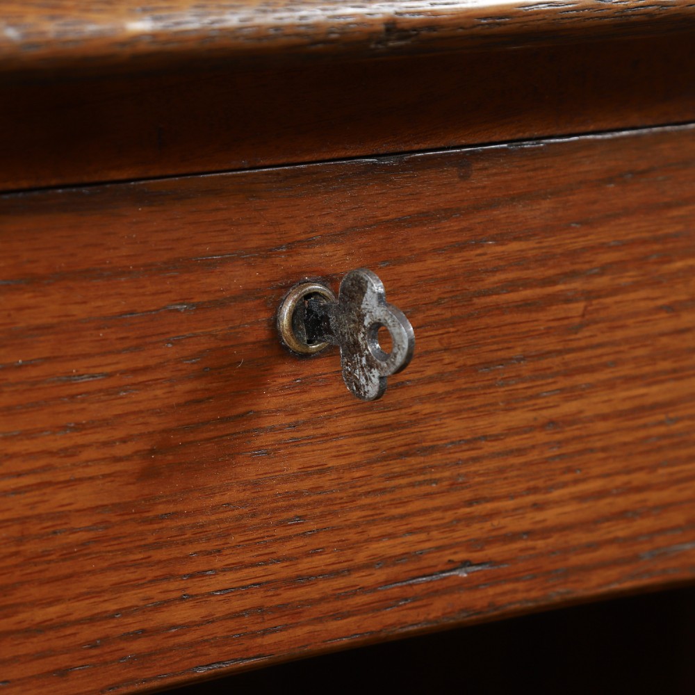 An Edwardian warm brown oak twin-pedestal rolltop desk featuring a flexible slatted wooden tambour shutter open to reveal internal pigeonholes above nine drawers with wooden cup handles. View V