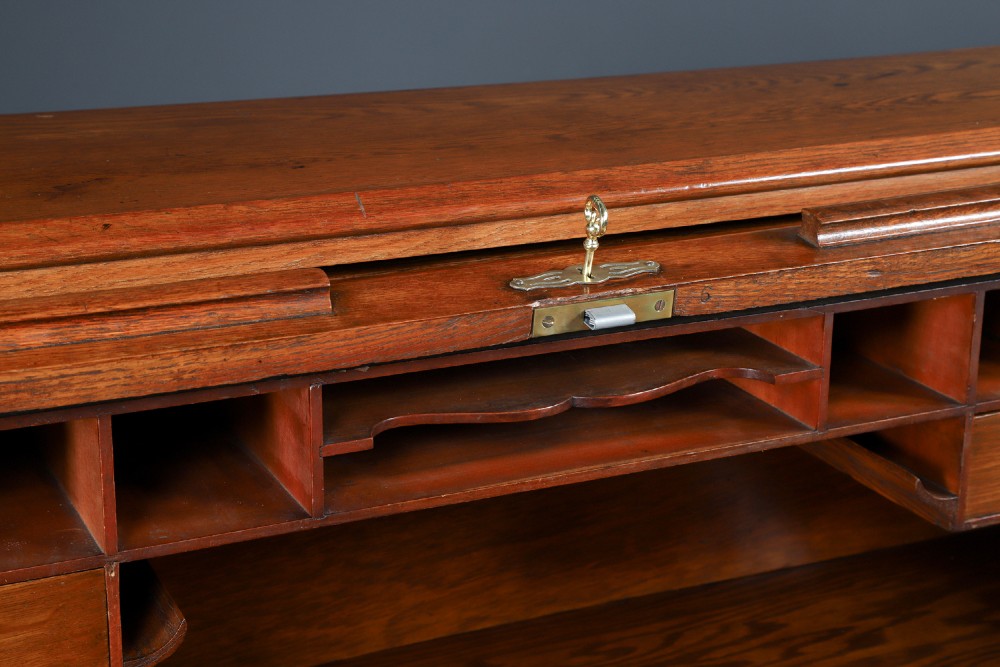 An Edwardian warm brown oak twin-pedestal rolltop desk featuring a flexible slatted wooden tambour shutter open to reveal internal pigeonholes above nine drawers with wooden cup handles. View VI