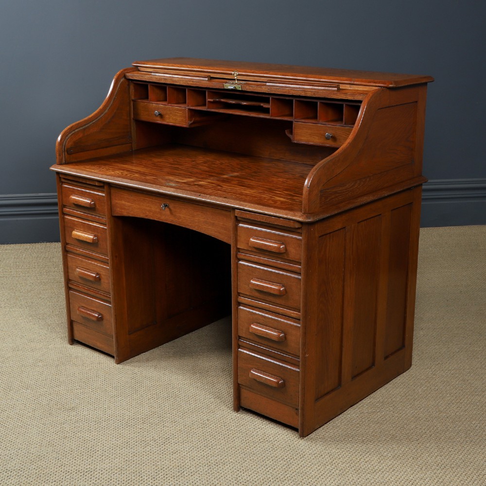 An Edwardian warm brown oak twin-pedestal rolltop desk featuring a flexible slatted wooden tambour shutter open to reveal internal pigeonholes above nine drawers with wooden cup handles. View IX