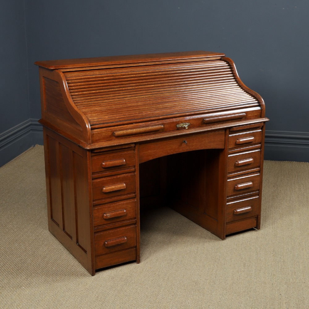 An Edwardian warm brown oak twin-pedestal rolltop desk featuring a flexible slatted wooden tambour shutter open to reveal internal pigeonholes above nine drawers with wooden cup handles. View X