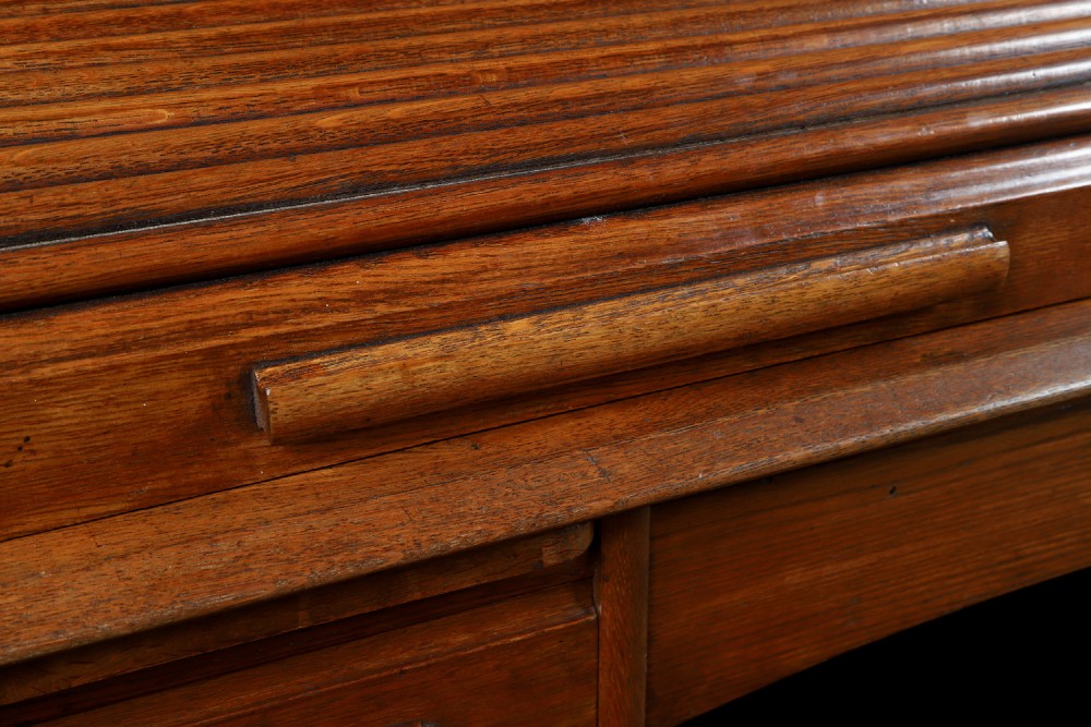 An Edwardian warm brown oak twin-pedestal rolltop desk featuring a flexible slatted wooden tambour shutter open to reveal internal pigeonholes above nine drawers with wooden cup handles. View XI