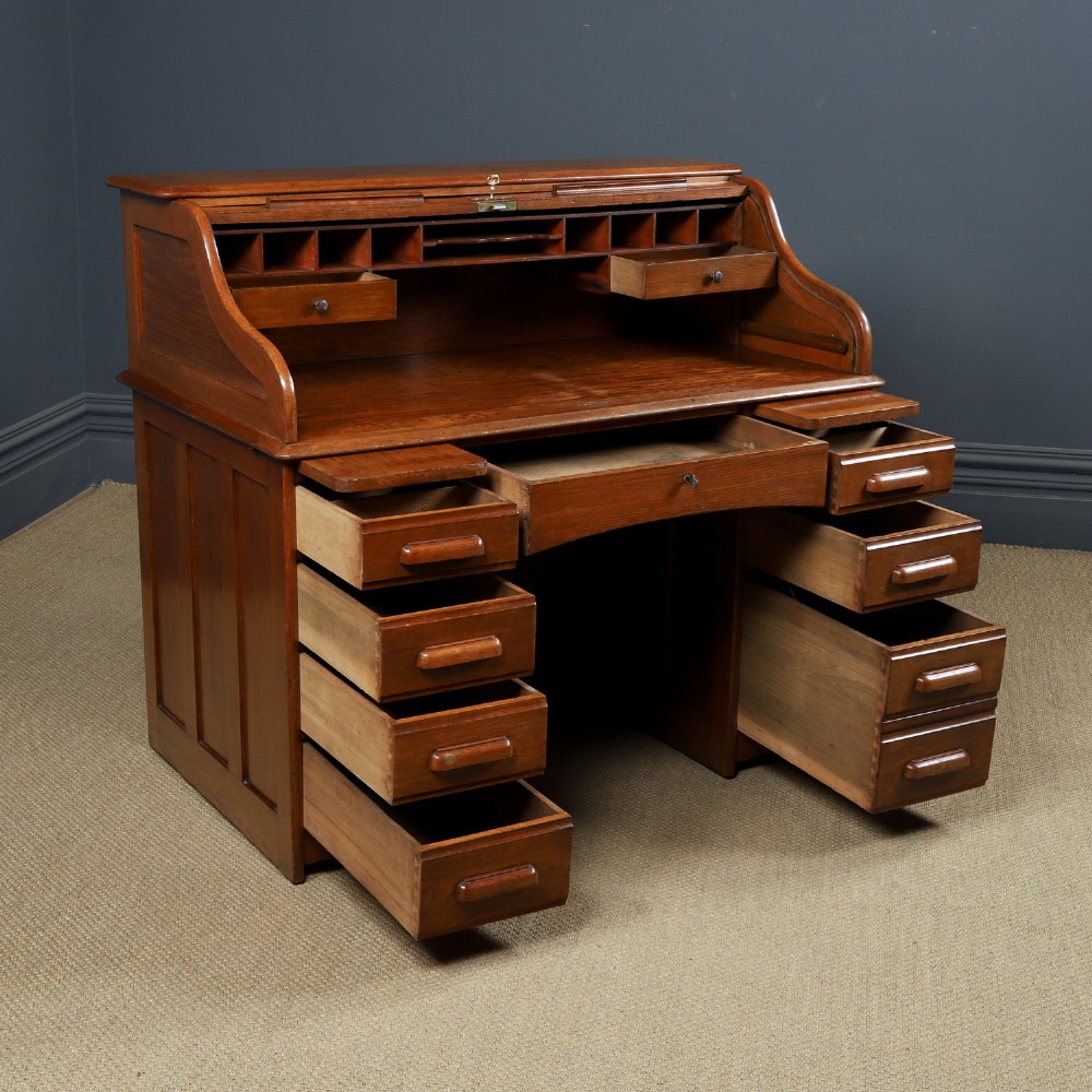 An Edwardian warm brown oak twin-pedestal rolltop desk featuring a flexible slatted wooden tambour shutter open to reveal internal pigeonholes above nine drawers with wooden cup handles. View XII
