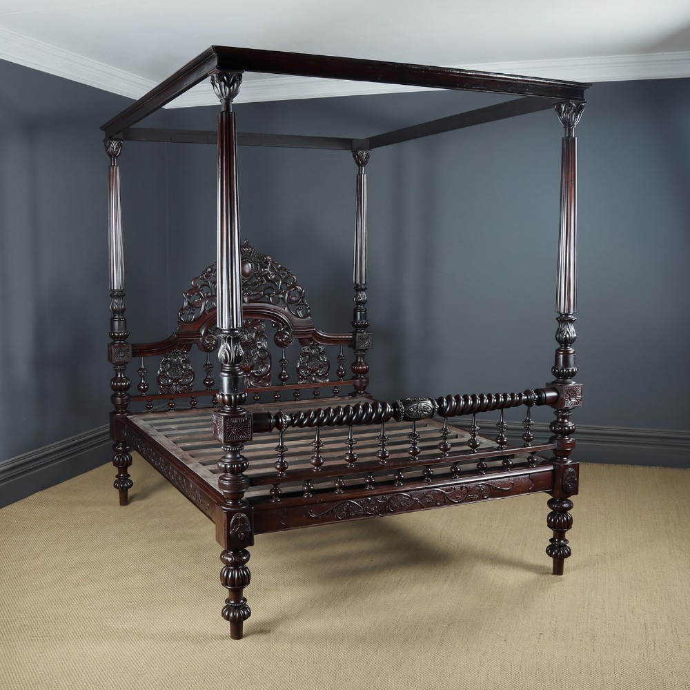 An Anglo-Indian mahogany four poster bed featuring carved turned posts, an ornate headboard, and a spindle footboard.