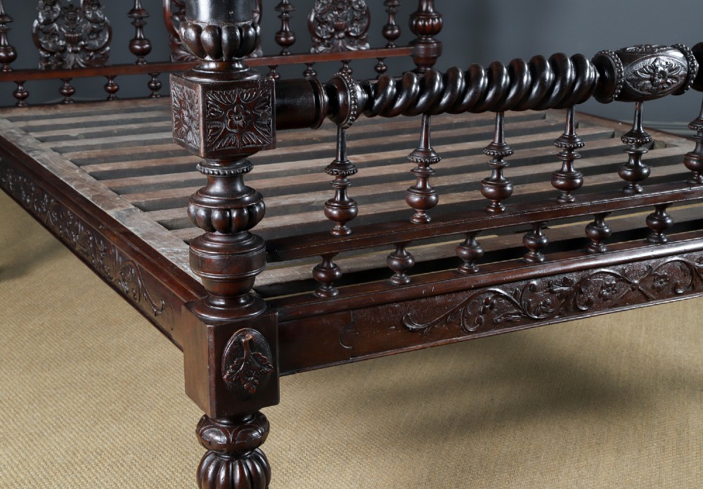 An Anglo-Indian mahogany four poster bed featuring carved turned posts, an ornate headboard, and a spindle footboard. View II
