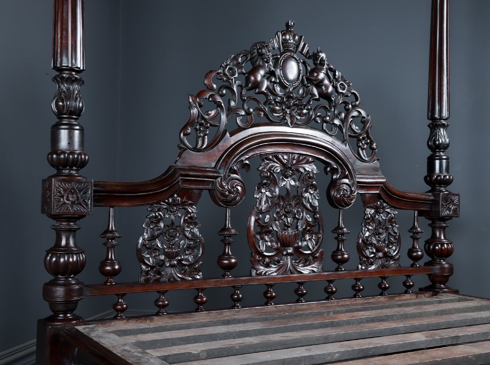 An Anglo-Indian mahogany four poster bed featuring carved turned posts, an ornate headboard, and a spindle footboard. View X