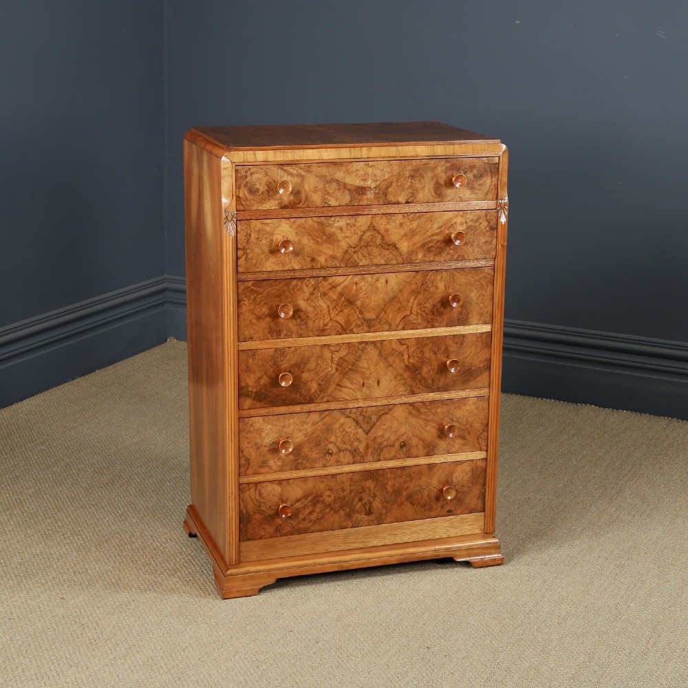 An Art Deco chest of drawers in figured burr walnut featuring six graduated drawers with turned wooden handles and carved shoulder details. View II