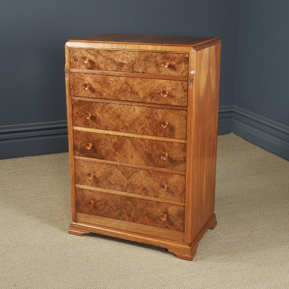 An Art Deco chest of drawers in figured burr walnut featuring six graduated drawers with turned wooden handles and carved shoulder details. View VIII